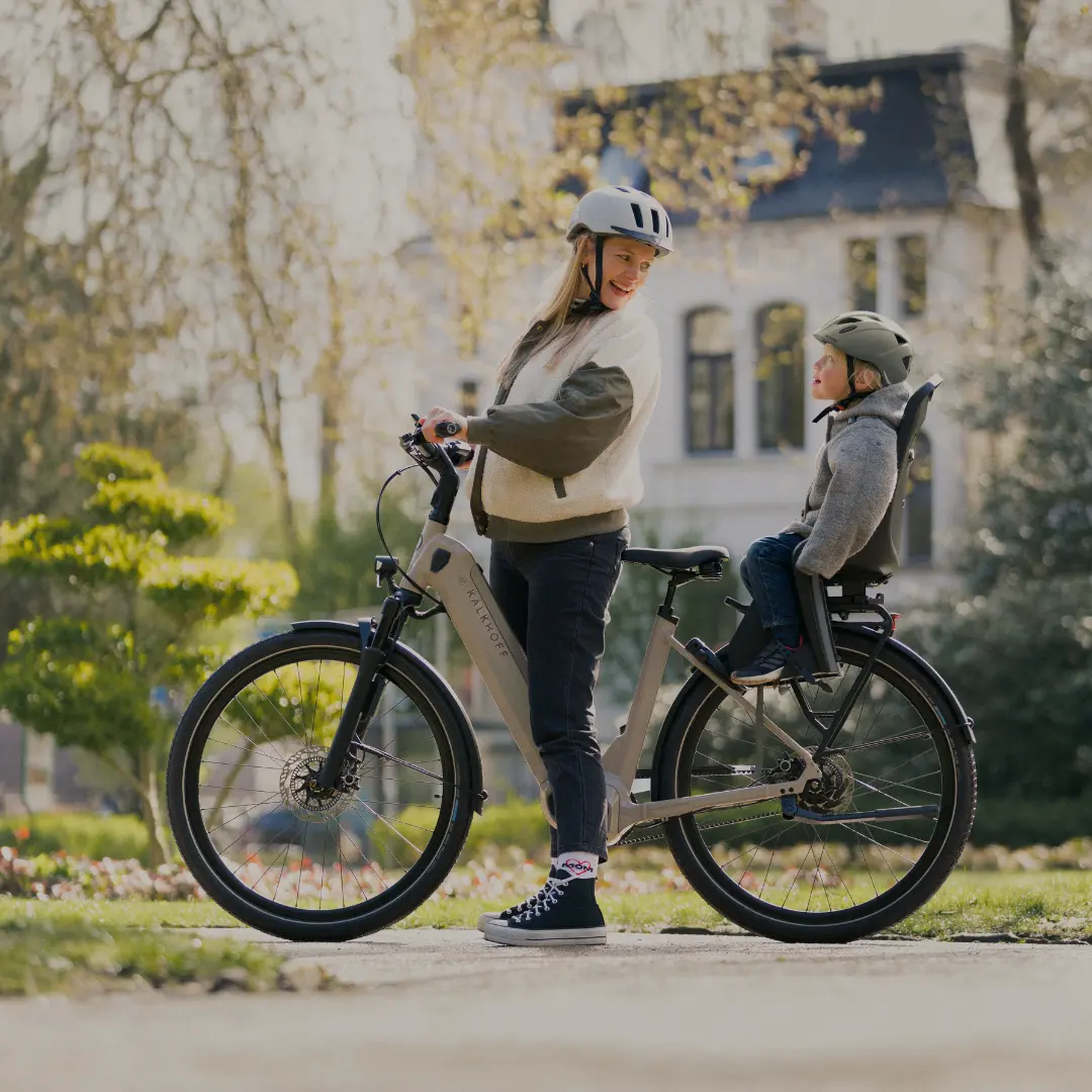 Frau mit Kind im Kindersitz auf einem E-Bike im Park