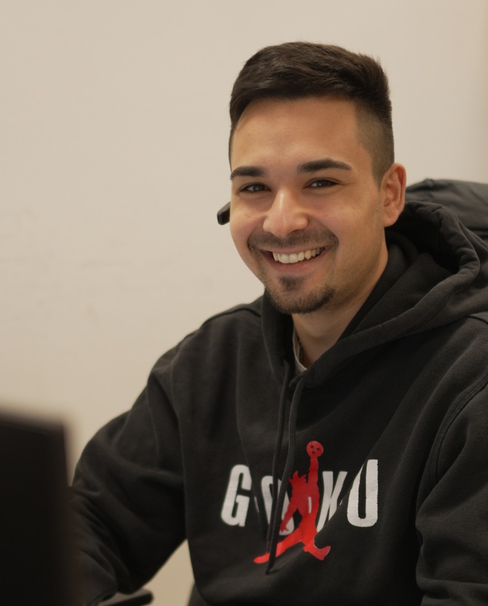 Lächelnder Servicemitarbeiter mit Headset am Schreibtisch – trägt schwarzen Goku-Hoodie.